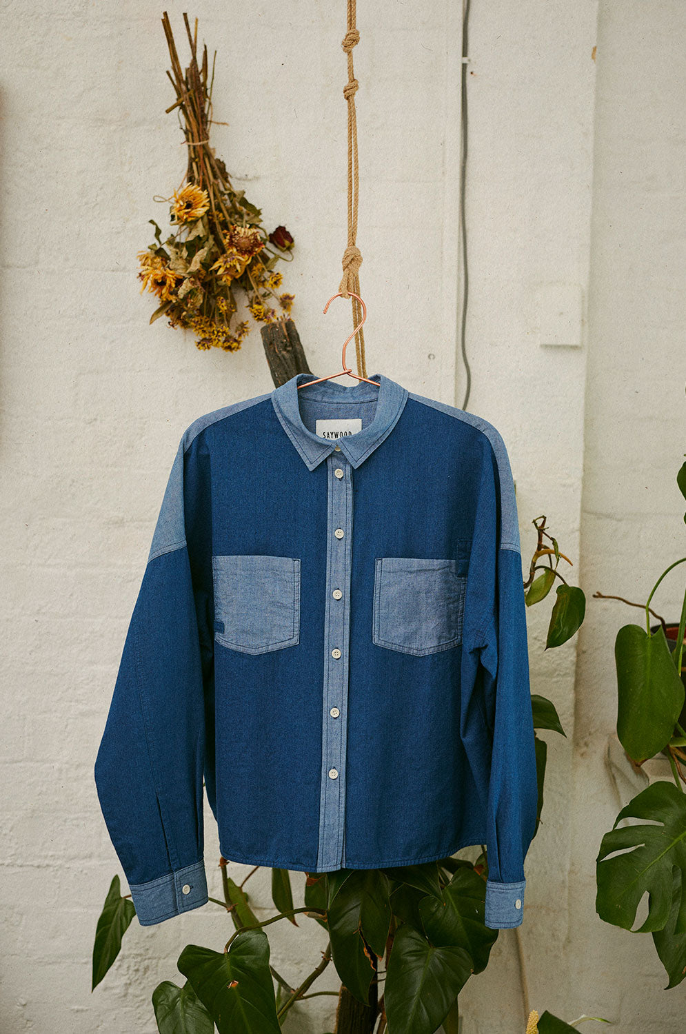 Lela patchwork Japanese denim shirt hanging on rose gold hanger with plants
